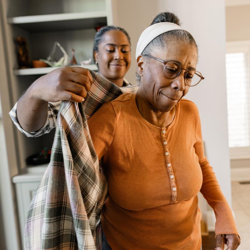 Hija ayudando a su madre anciana a ponerse el abrigo