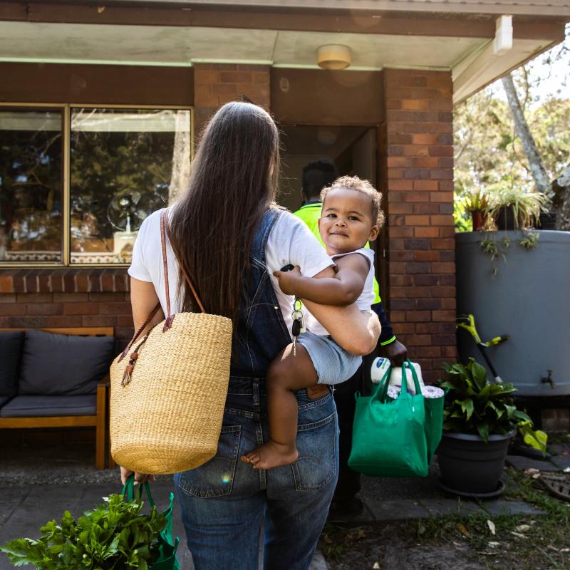 Madre sosteniendo a su hija caminando hacia la puerta principal.